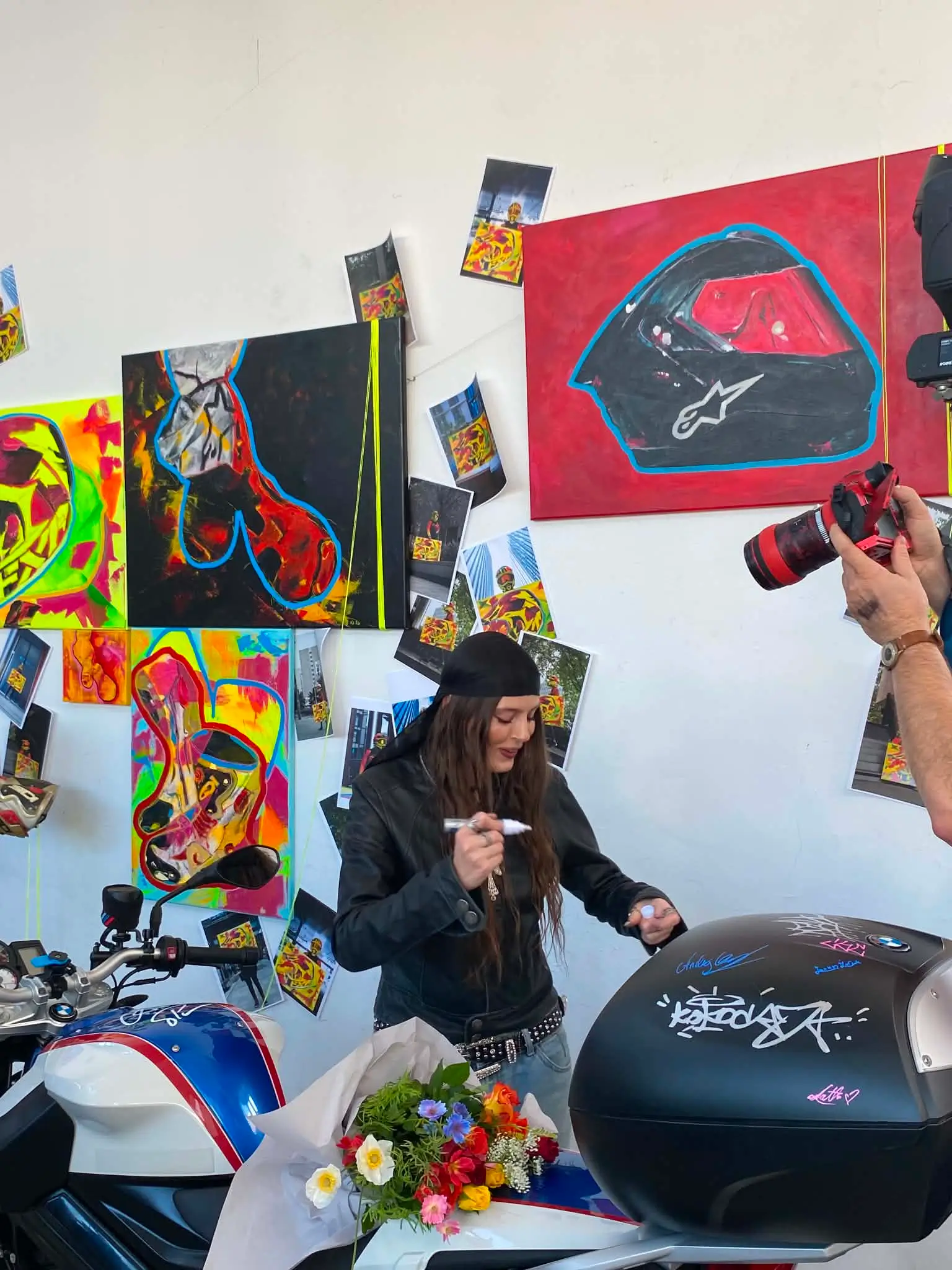 Odwiedzająca zostawia podpis markerem na kufrze motocykla BMW na tle obrazów z kaskami, Fashion Is Art Warsaw