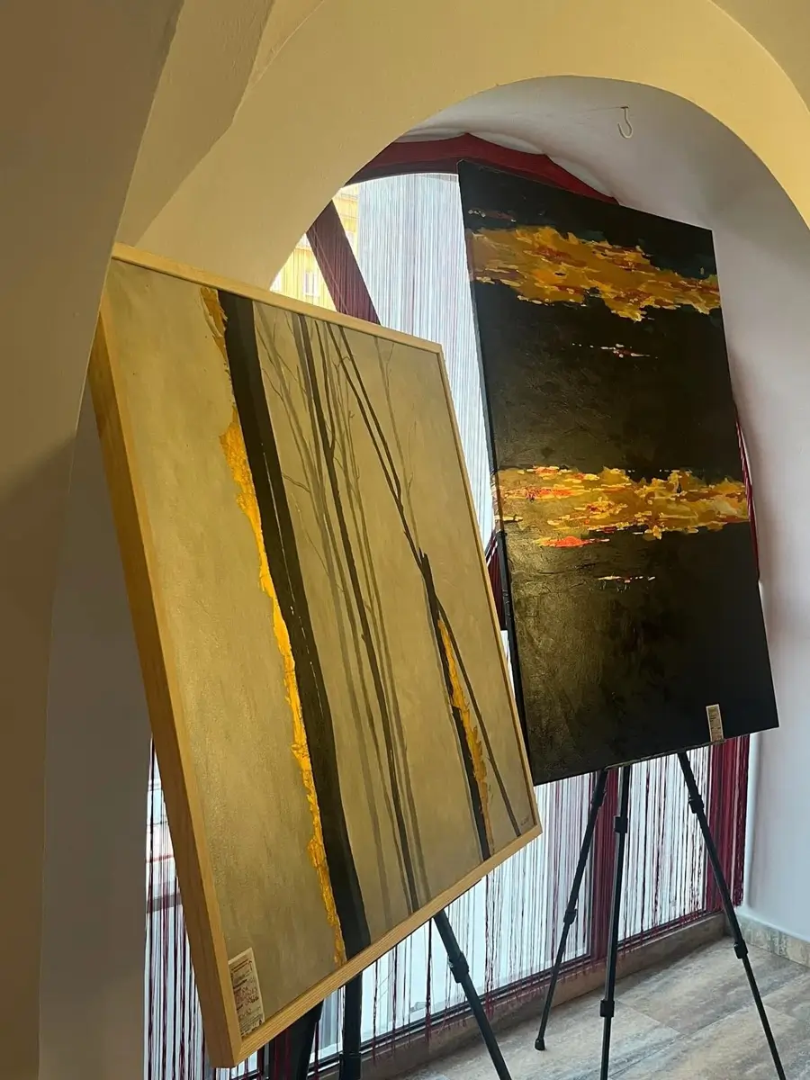 Two paintings with gold accents on easels under an arched window, exhibition at Wernisaż Café & Bar